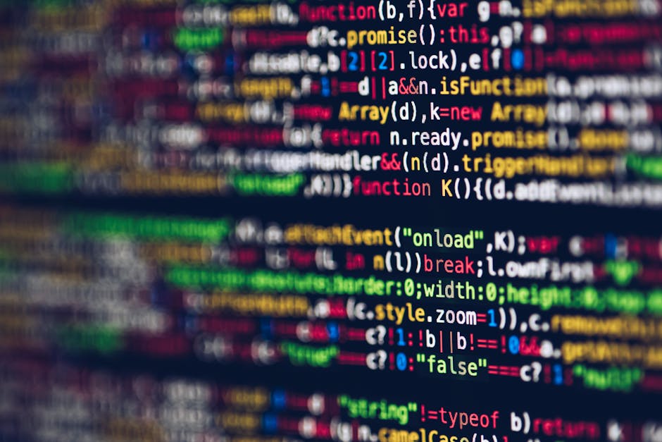 A close-up photograph of a computer screen displaying colourful programming code with syntax highlighting in shades of green, blue, purple, and pink, set against a dark background. The screen's surfac